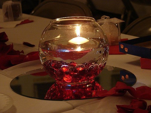 floating candle in glass holder with red pebbles and stones on a mirror wedding centerpieces