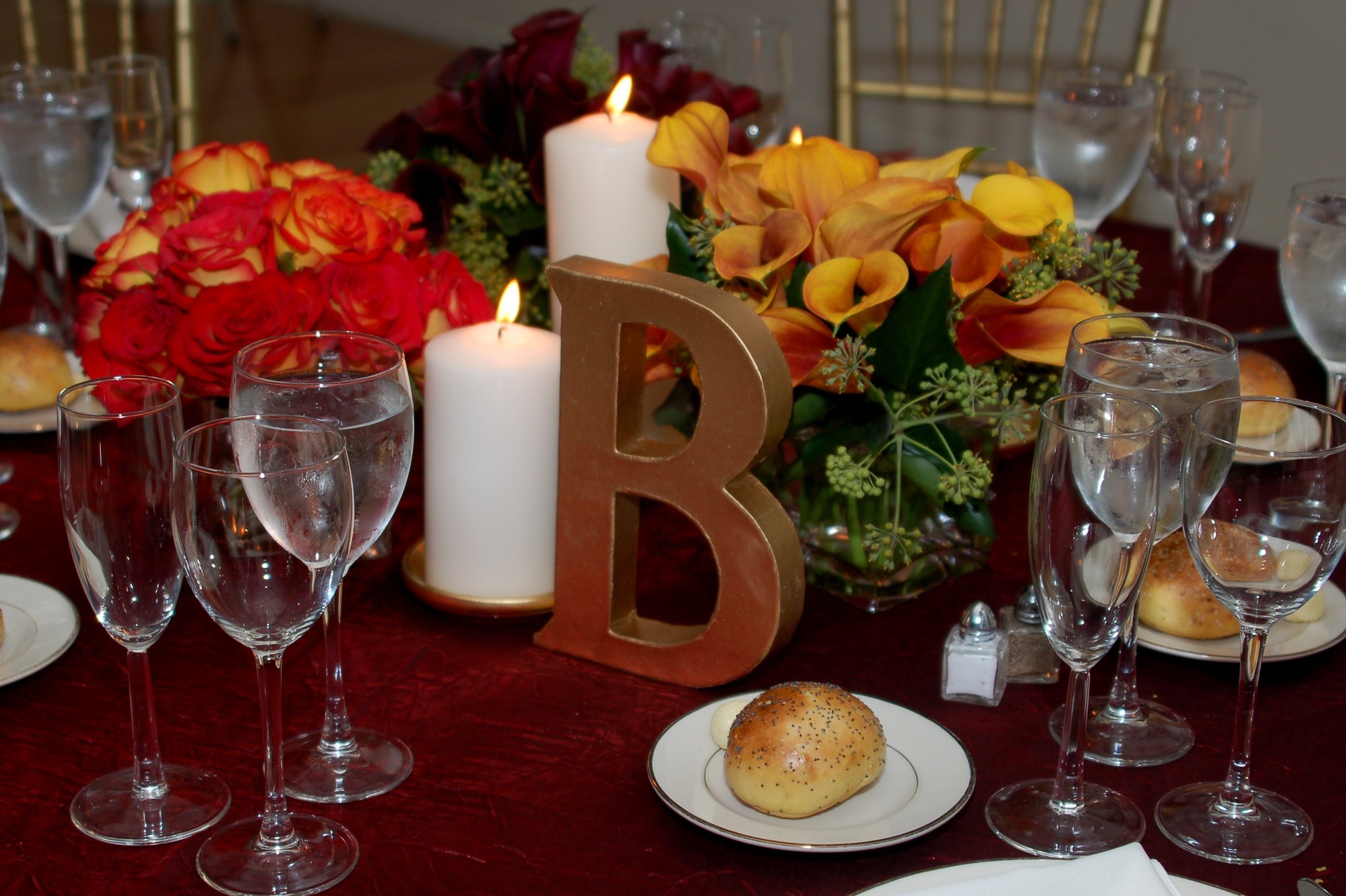 Beautiful Fall Wedding Reception Table With Large White Candles and Festive Flowers with orange, red and yellow autumn colors showing