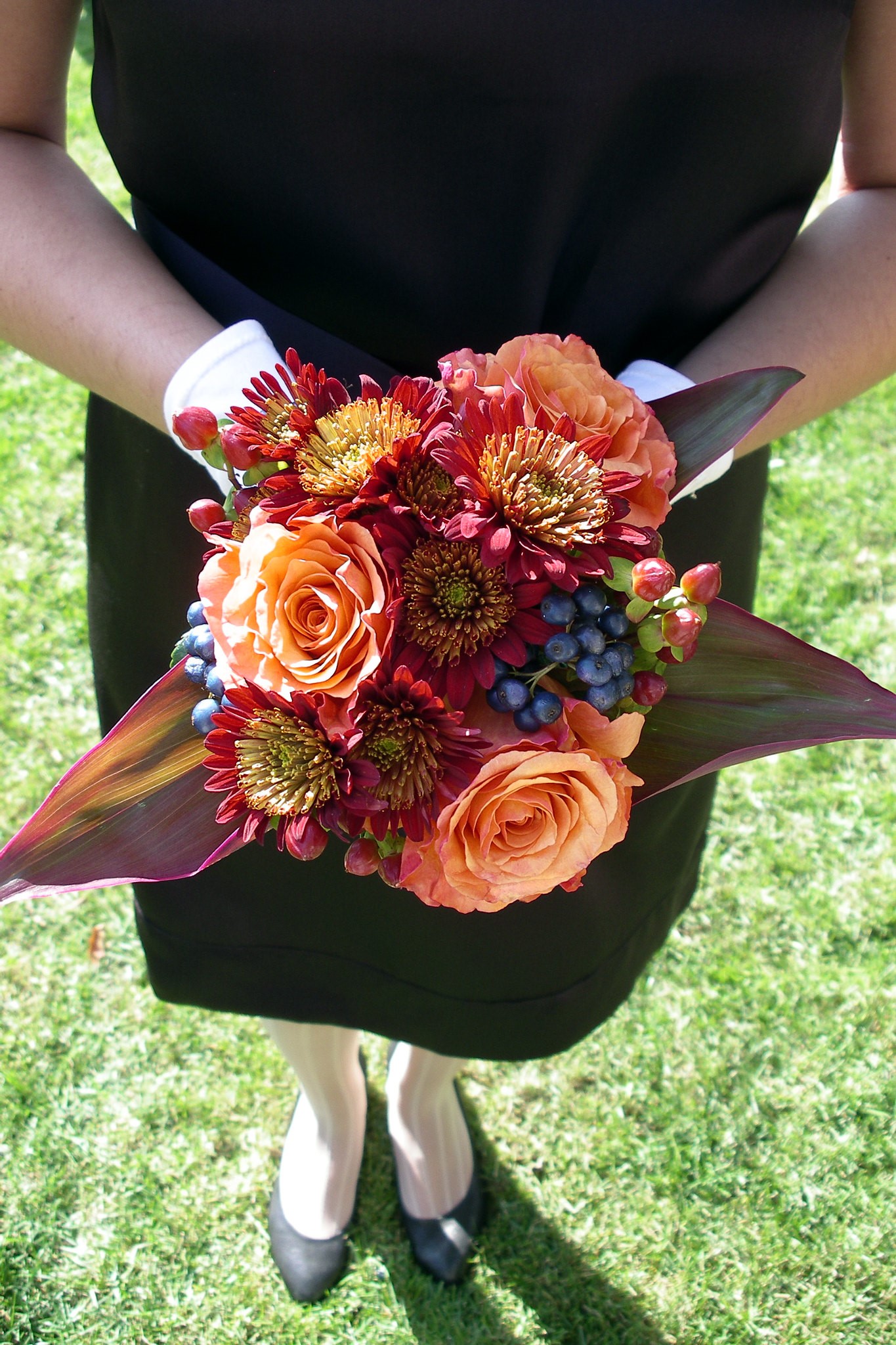 Bridesmaid in Black holding gorgeous bouquet of orange and red flowers accented with green and purple