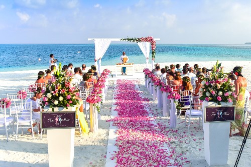 Beautiful Beach Wedding Ceremony With White Bridal Arch and White Aisle Covered in Pink Flower Petals