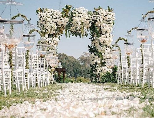 White outdoor wedding Ceremony with white chairs and a huge bridal arch covered in white flowers, white flowers on the wedding aisle.