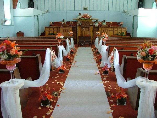 Beautiful Fall Wedding in a Church with large fall themed floral arrangements, white ribbon draped across the pews and smaller floral arrangements at ground level with fall colored flower petals