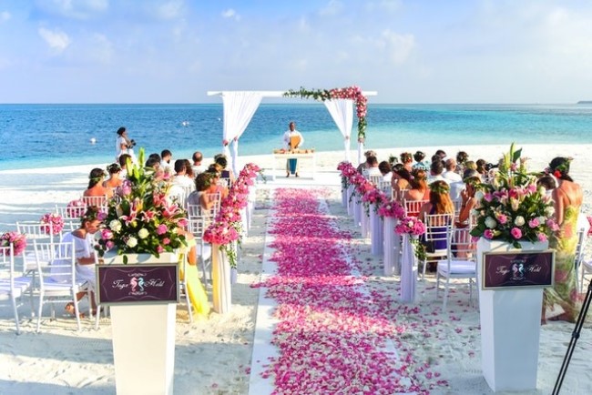beautiful outdoor wedding ceremony at the beach with white bridal arch and pink petals on wedding aisle